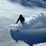 An off-piste skier in deep powder makes a big snow rooster tail, whilst cat skiing in Georgia