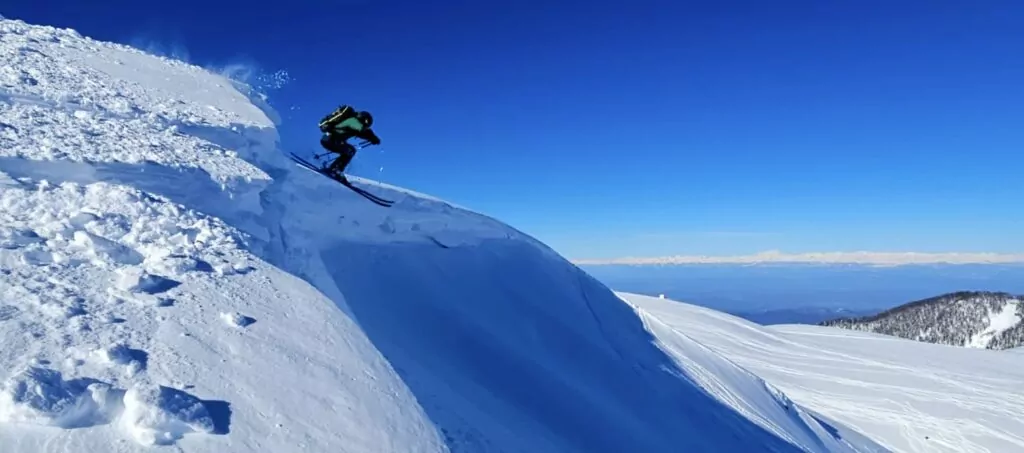 Georgian mountain guide skiing off a drop into deep snow below