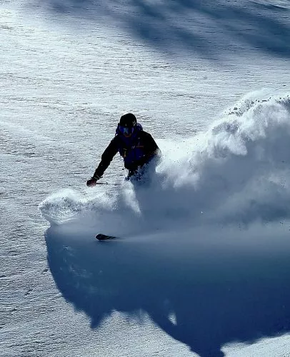 An off-piste skier in deep powder makes a big snow rooster tail, whilst cat skiing in Georgia